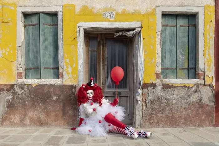 Framed Print : A woman dressed as a clown holds a ballon in front of a colourful facade on Burano Framed Print : A woman dressed as a clown holds a ballon in front of a colourful facade on Burano
