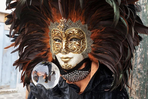 A woman in a feather Venetian mask poses with a glass ball during the Venice Carnival
