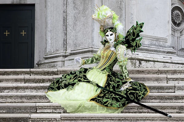 Woman in green costume at Carnival time sitting on steps at Salute, Venice, Veneto, Italy