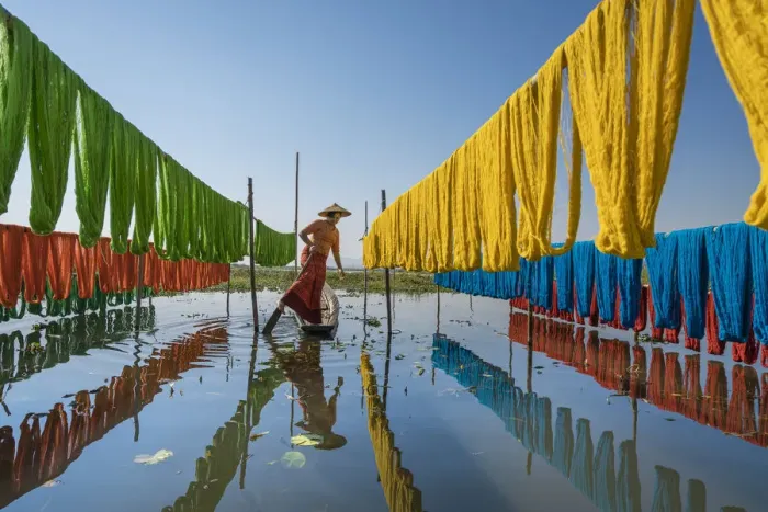 Framed Print : Woman hanging dyed yarn from a boat to dry in a traditional weaving village on Lake Inle