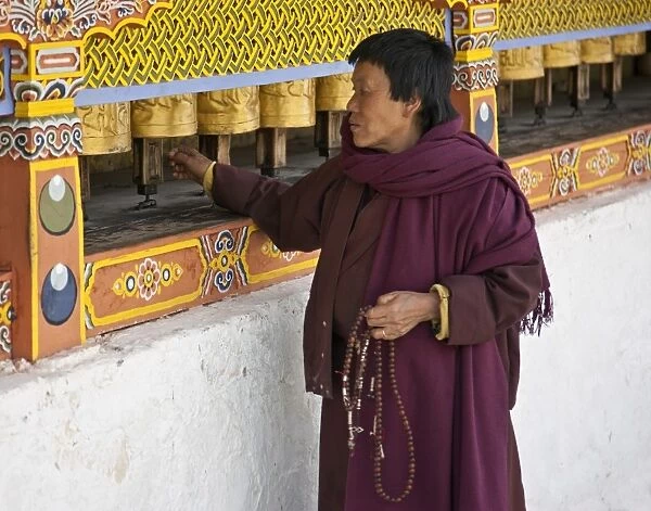A woman, prayer beads in hand, spins brass prayer wheels as she mutters an invocation to protective deities at the 18th century Chorten Kora in