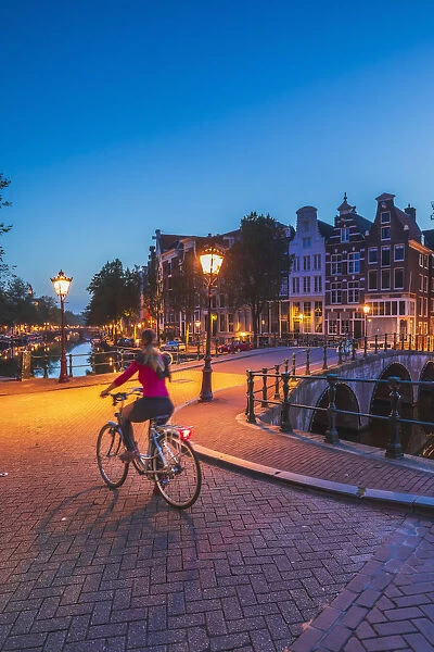 A woman riding a bike by night in Amsterdam along Keizersgracht canal in Amsterdam