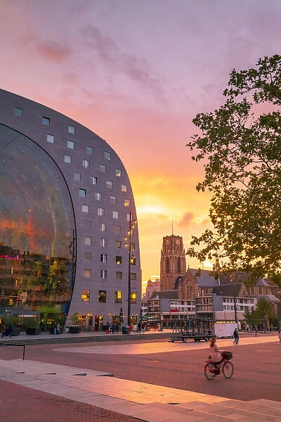 A woman riding a bike at sunset in front of the Market Hall in Rotterdam on a summer