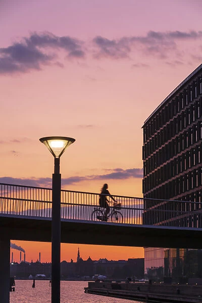 A woman riding a bike on a suspended bridge in Copenhagen at sunset, Denmark