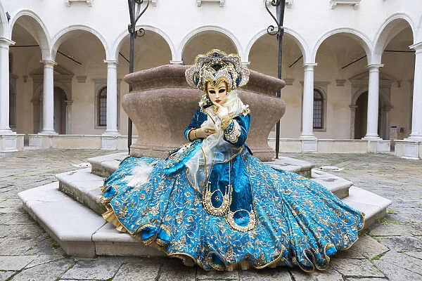 A woman sits in a magnificent costume in front of a well during the Venice Carnival