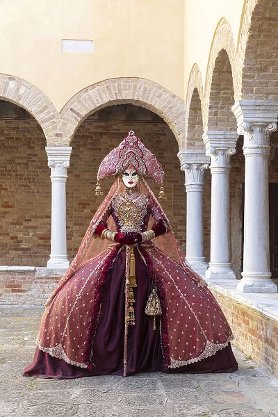 A woman wearing an Indian style costume and mask poses in the cloisters of Chiesa di San