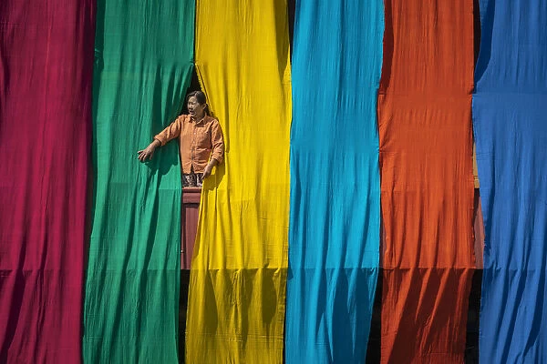 Woman in a window checking freshly dyed fabric hanging from bamboo poles to dry on a