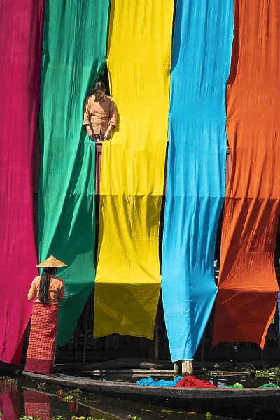 Two women checking freshly dyed fabric hanging from bamboo poles on a house to dry