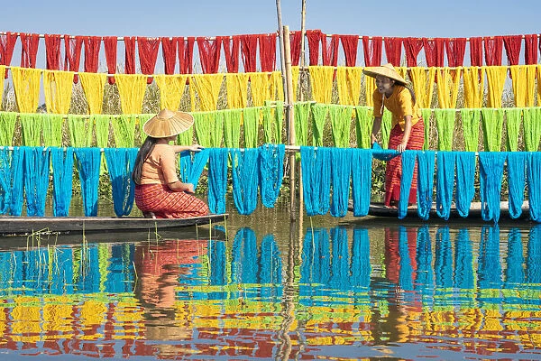 Two women hanging dyed yarn from boats to dry in a traditional weaving village on Lake