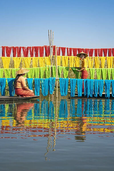 Two women hanging dyed yarn from boats to dry in a traditional weaving village on Lake