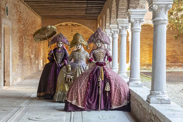 Three women wearing Indian style costumes and masks pose in the cloisters of Chiesa di