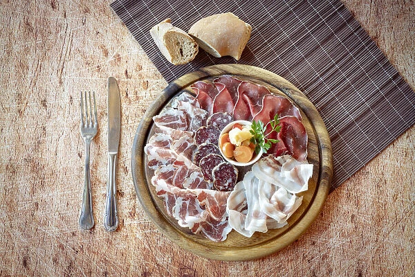 Wood chopping board with mixed italian cold cuts appetizer and cutlery from above