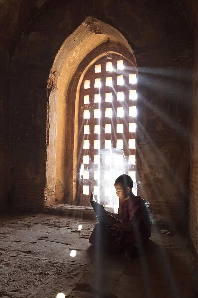 Young Buddhist monk reads by a window in a temple in Bagan, Myanmar