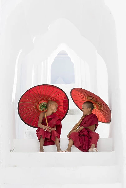 Two young Buddhist monks holding red umbrellas have fun in Hsinbyume Pagoda, Mingun