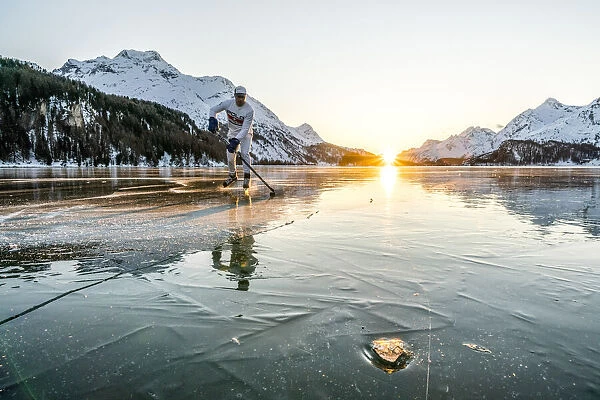 Young man playing ice hockey on frozen Lake Sils at sunset, Graubunden, Engadine