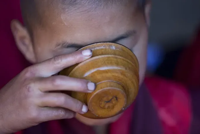 Framed Print : A young monk drinking milk from a wooden bowl in Bhutan