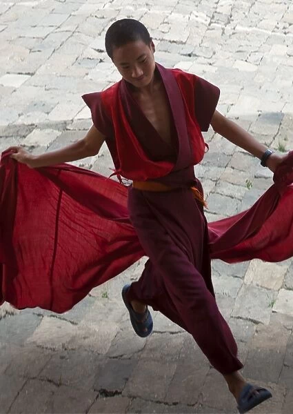 A young monk holds his red robes as he runs across the courtyard of Wangdue Phodrang Dzong