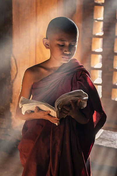 A young monk reading by a window inside a temple, UNESCO, Bagan, Mandalay Region, Myanmar