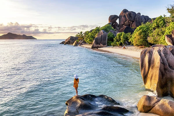 A young woman admires the sunset at Anse Source d Argent, La Digue, Seychelles, Africa