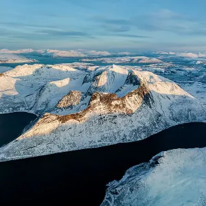Aerial view of Oksfjord village and Grytetippen mountain covered with snow overlooking the cold sea, Senja, Troms county, Norway Aerial view of Oksfjord village and Grytetippen mountain covered with snow overlooking the cold sea, Senja, Troms county, Norway