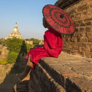 Bagan, Mandalay region, Myanmar (Burma). A young monk with red umbrella watching