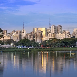 Brazil, Sao Paulo, Sao Paulo City, urban city skyline reflected in the lake in Ibirapuera Park. Copy space, no people, golden evening light