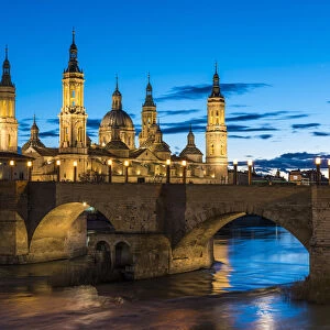 Cathedral of Our Lady of the Pillar and stone bridge at dusk. Zaragoza, Aragon, Spain