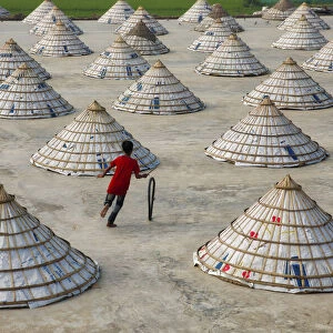Children weave in and out of scores of giant cones as they roll bike tyres around a rice