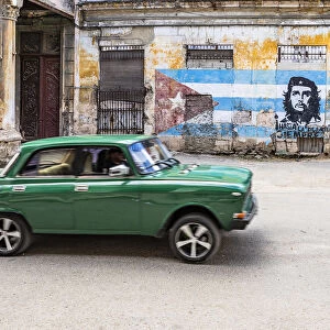 A classic car driving in a front of Che Guevara street art in La Habana Vieja (Old Town)
