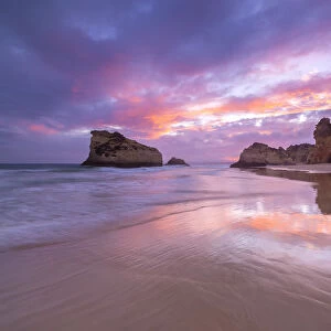 A colorful sunset reflected on the wet shores of Praia Dos Tres Irmaos