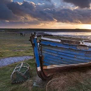 Decaying fishing boat on Holy Island at dawn, with Lindisfarne Castle beyond, Northumberland