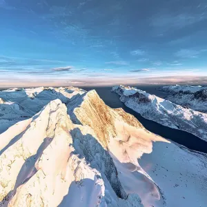 Dramatic sky at dawn over majestic Breidtinden mountain peak covered with snow, aerial view, Mefjorden, Senja, Troms county, Norway Dramatic sky at dawn over majestic Breidtinden mountain peak covered with snow, aerial view, Mefjorden, Senja, Troms county, Norway