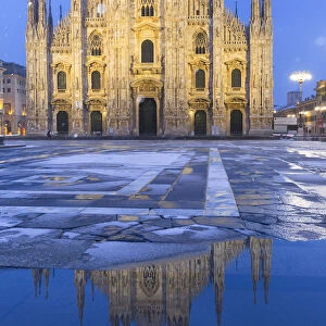 Duomo of Milan is reflected in a puddle during a snowfall at twilight. Milan, Lombardy