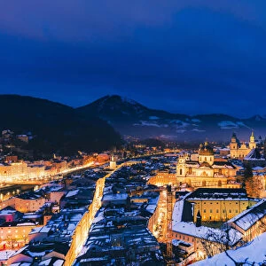 Elevated view of Salzburg city by night on a winter evening with the roofs covered