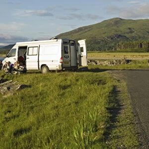A family on a camping holiday sit outside their campervan