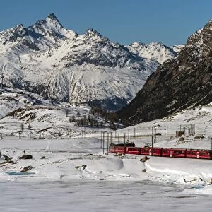 The famous Bernina Express red train passing Lago Bianco in a scenic winter mountain landscape