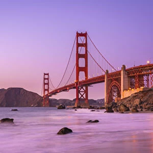 Famous Golden Gate Bridge over bay against purple sky during sunset, San Francisco