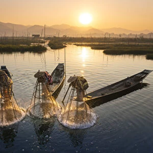 Three fishermen catching fish from boats using traditional conical nets at sunrise