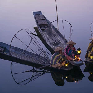 Three fishermen sitting on their boats warming up around a fire before sunrise, Lake Inle