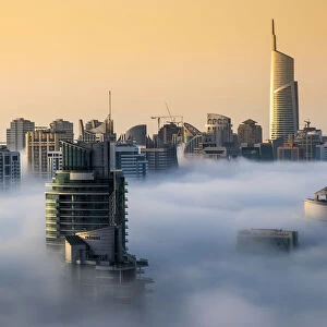 Foggy sunrise with Dubai Marinas skyscrapers towering over the low clouds