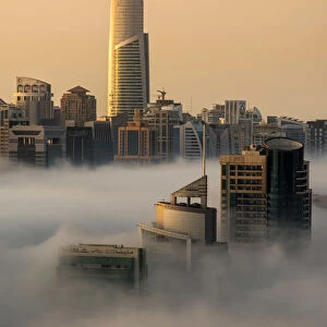 Foggy sunrise with Dubai Marins skyscrapers towering over the low clouds, Dubai