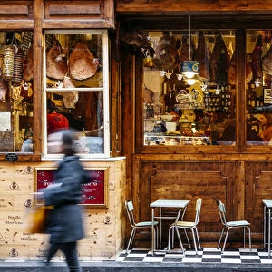 Girl reading in front of a traditional Salumeria in Bologna, Emilia Romagna, Italy