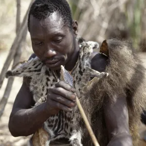 A Hadza hunter checks the straightness of a new arrow shaft