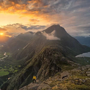 Hiker walking on Romsdalseggen ridge over Rauma valley lit by sun rays at sunset