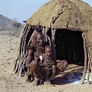 A Himba mother and baby son relax outside their dome-shaped home
