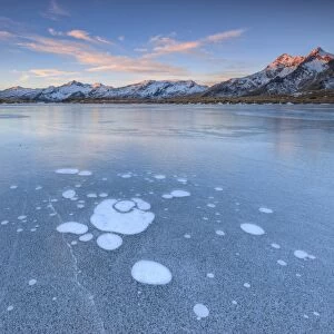 Ice bubbles on the frozen surface of Andossi Lake at sunrise Spluga Valley Valtellina