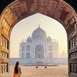 India, a beautiful woman in a red and yellow sari in front of the Taj Mahal at sunrise