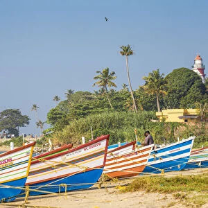 India, Kerala, Kollam, Fishing boats on beach with Tangasseri Lighthouse in background