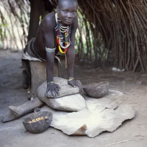 A Kwego woman grinds sorghum flour at the entrance to her hut