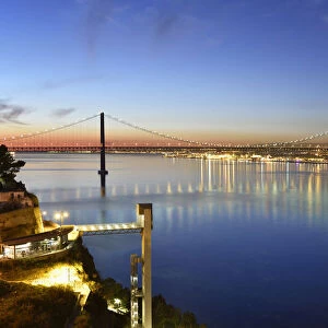 Lisbon and 25 de Abril bridge over the Tagus river, at dusk, seen from Almada. Portugal